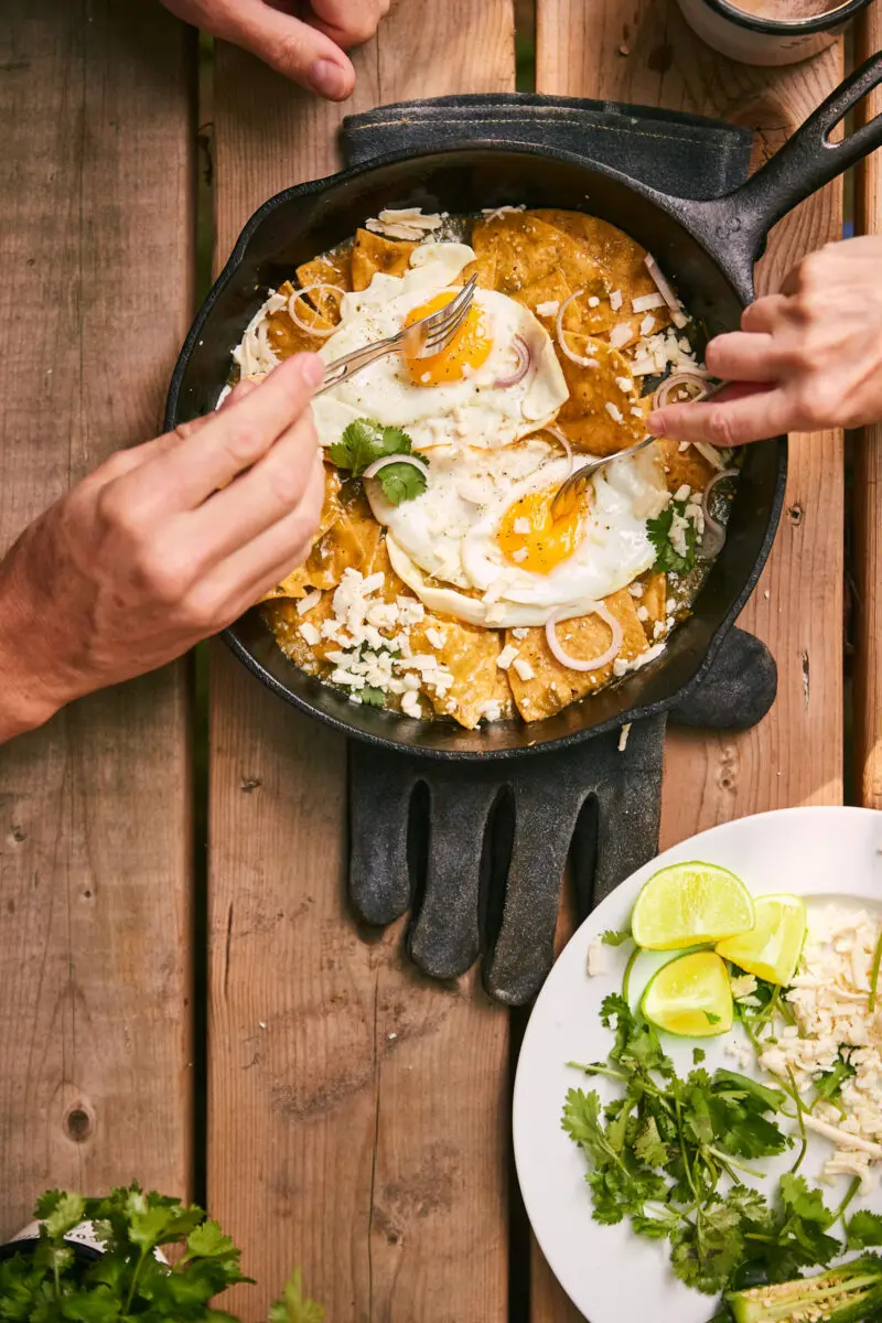 Campfire chilaquiles verdes in a cast iron pan, corn chips coated in salsa verde and topped with a fried egg