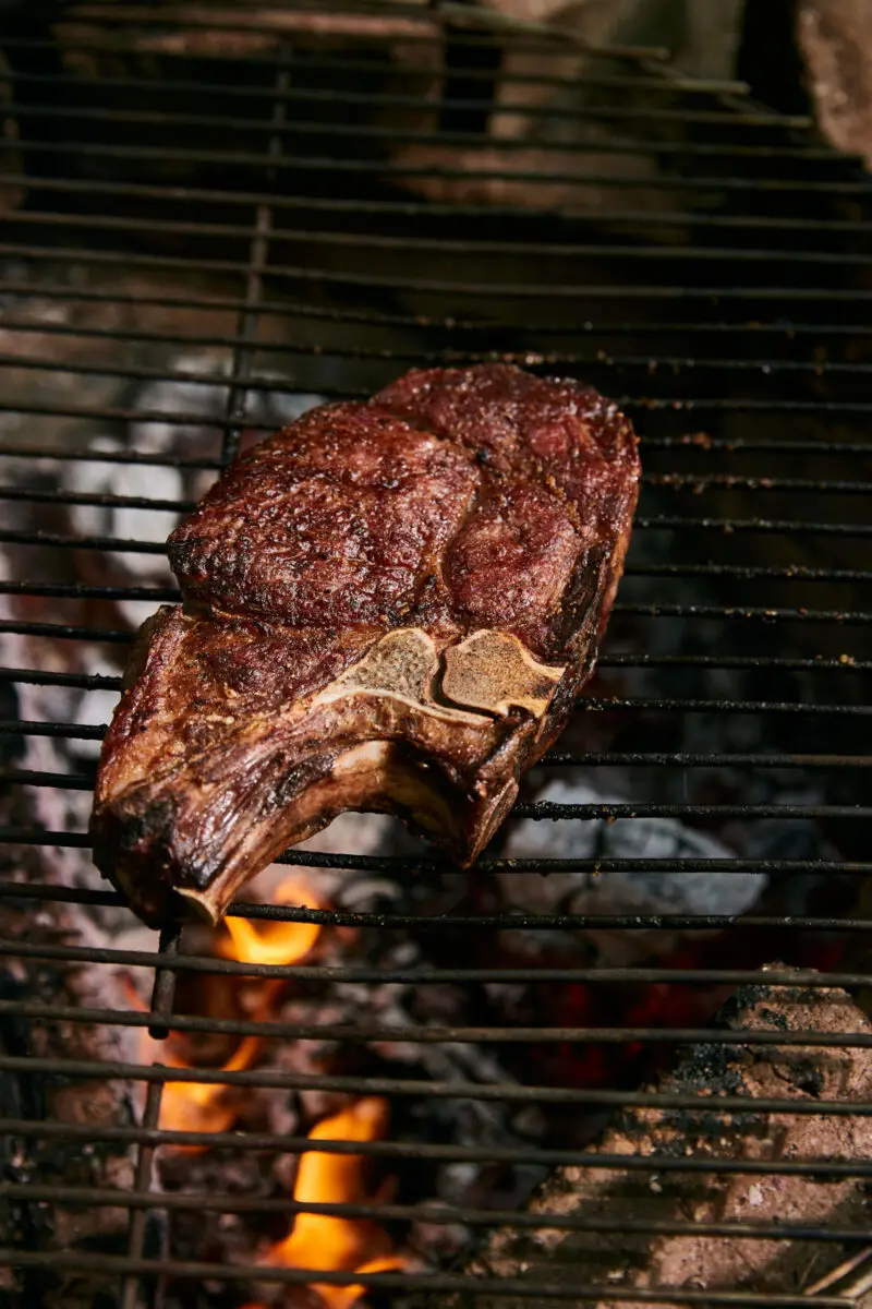 Thick bone-in steak searing on a grate over hot coals