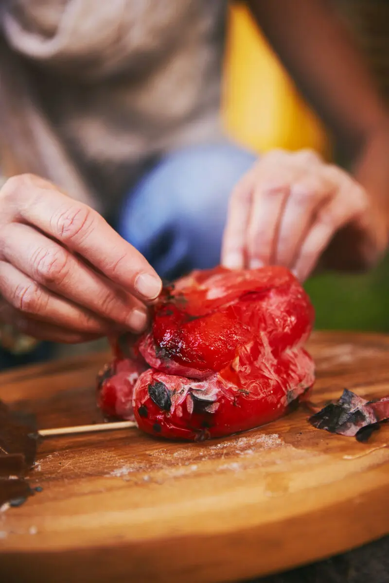 Peeling the blistered skin off a pepper roasted in the embers