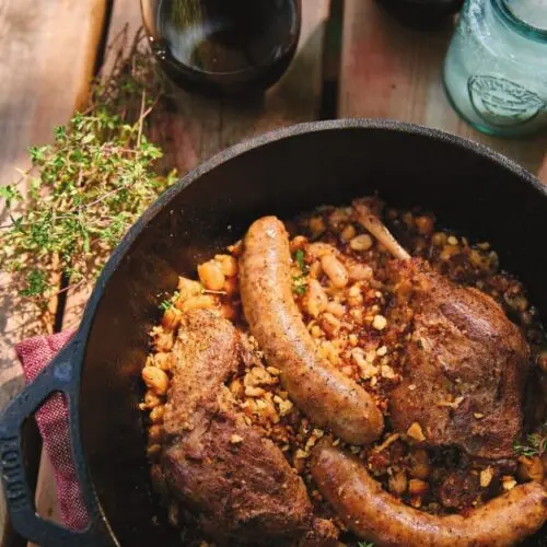 Campfire cassoulet in a cast iron pot with duck confit, Toulouse sausage and cannellini beans under garlic breadcrumbs
