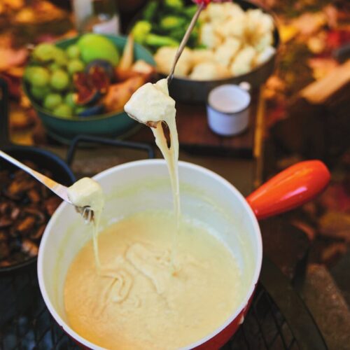 Campfire cheese fondue bubbling in a caquelon over embers, bread cubes on forks alongside