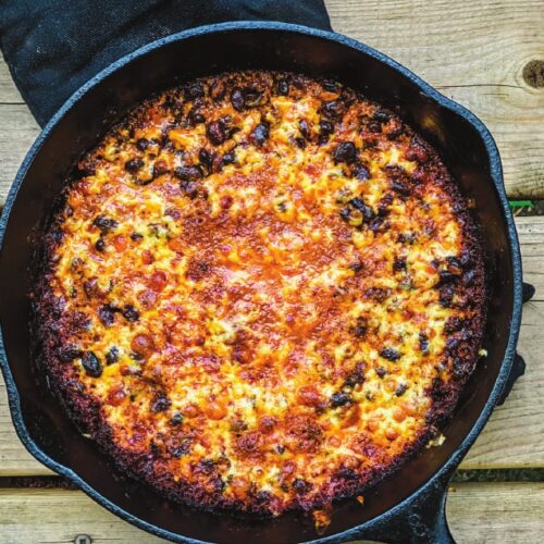 Beans au gratin in a cast iron pan, black beans under a torched golden cheese crust over the fire