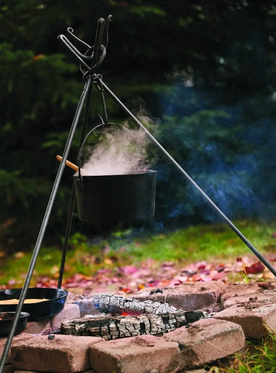 A cast iron pot steaming on a tripod over the campfire coals