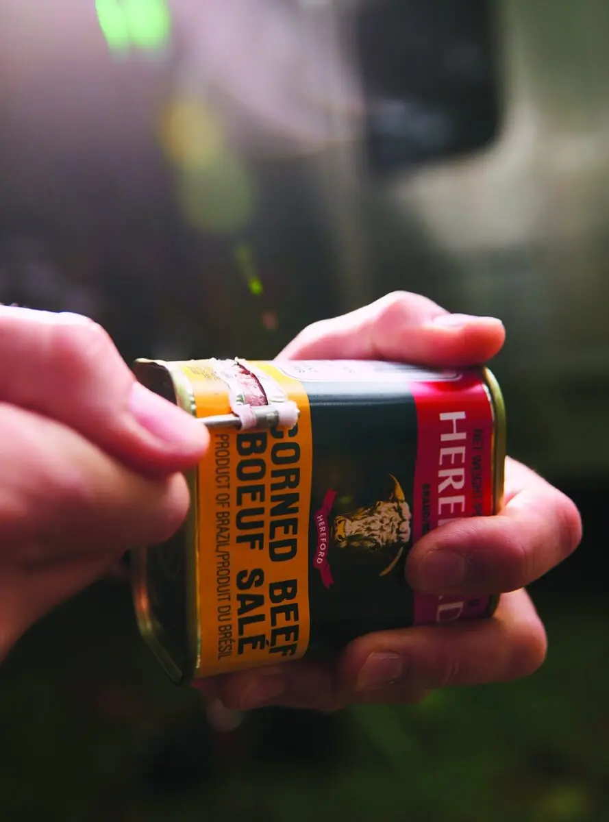 A can of corned beef held in hand before making campfire corned beef hash