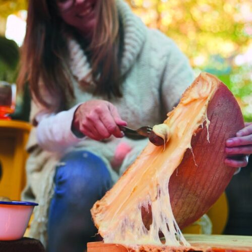 Scraping melted fireside raclette off the wheel onto a board