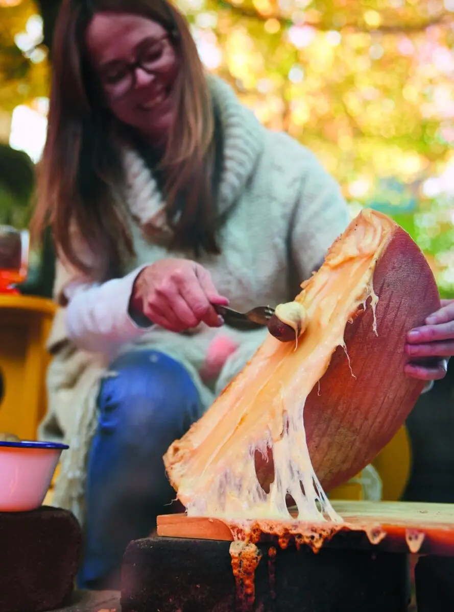 Scraping melted fireside raclette off the wheel onto a board