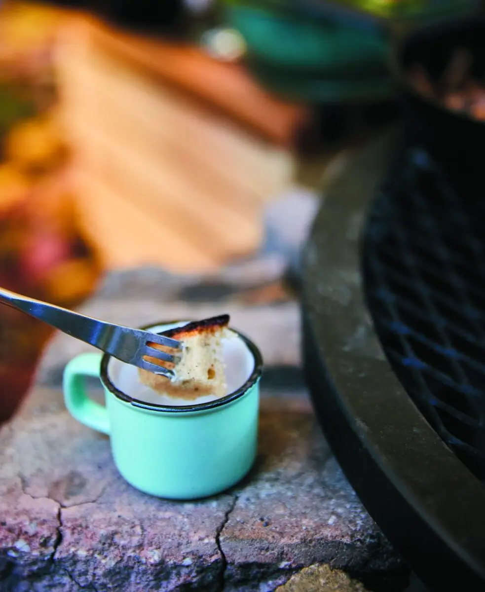 Campfire Cheese Fondue 3 Dipping a piece of bread into a mug of campfire cheese fondue